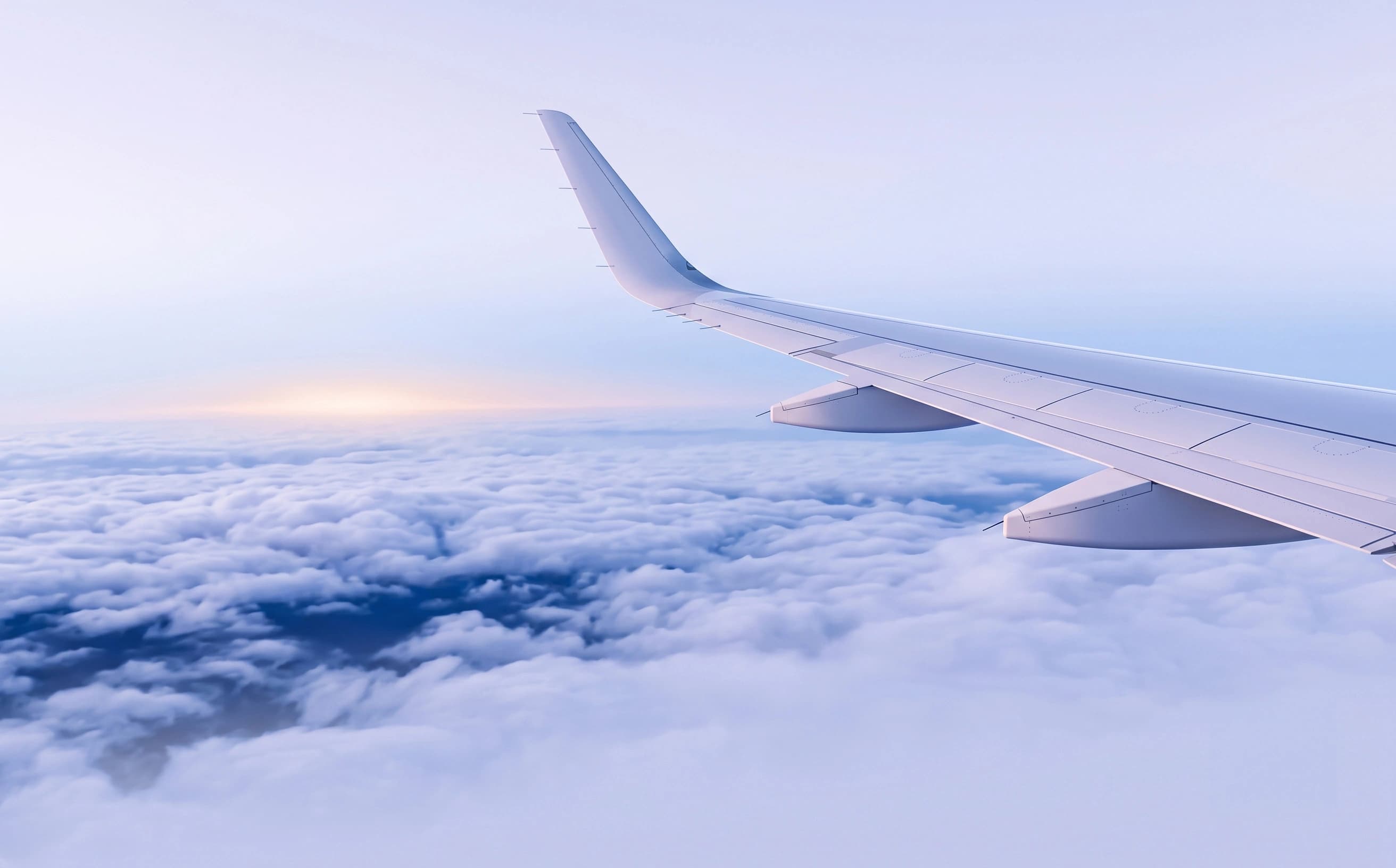 Airplane wing above sunrise clouds